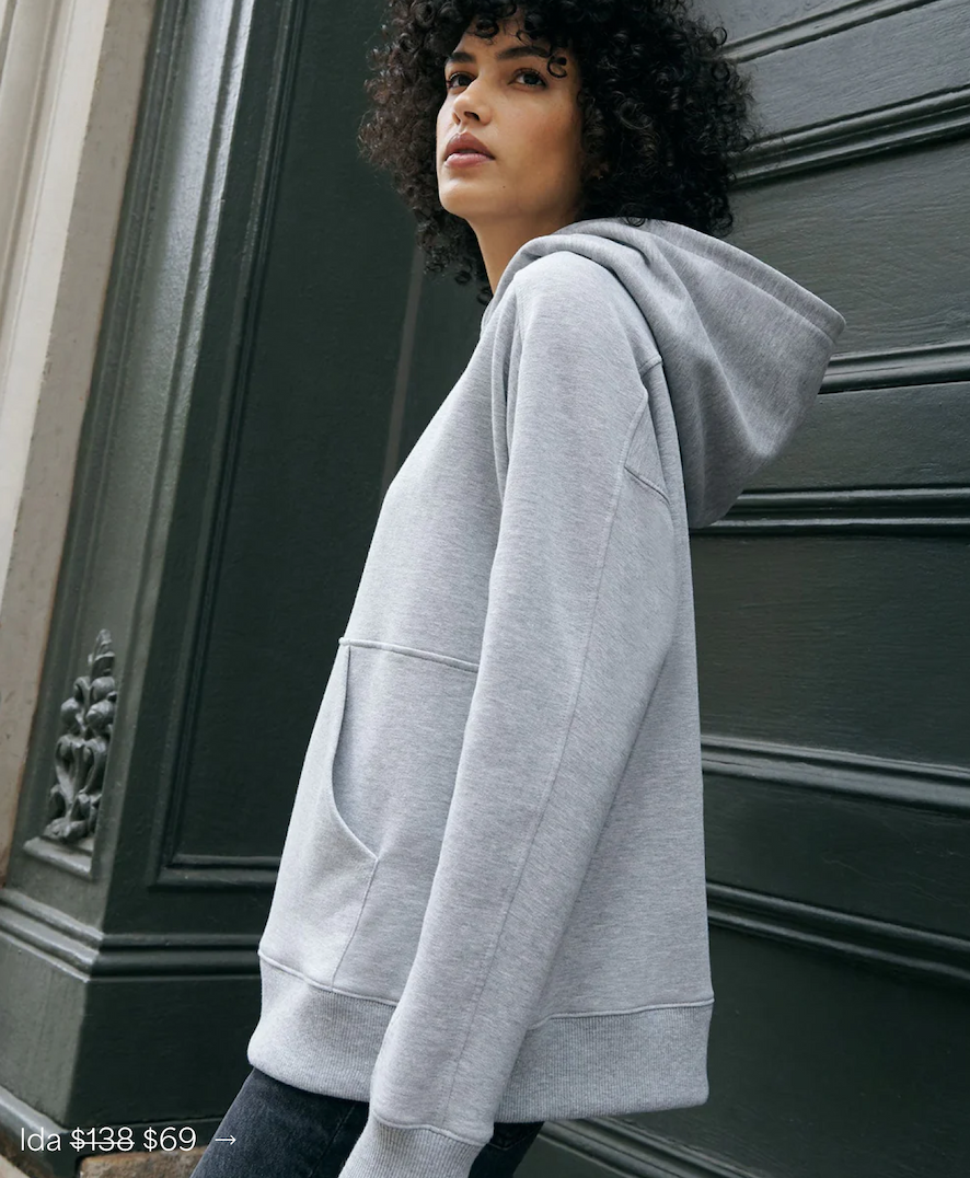 Astrid in The Ida Hoodie with a kangaroo pocket with her side facing the camera, in a dark paneled wall.