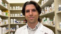Isaac Robinson stands with white Giant Pharmacy coat, with shelves of medication behind him