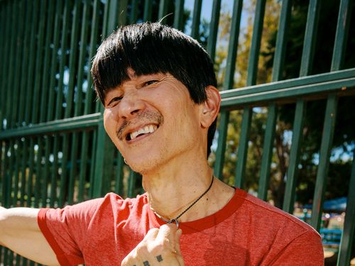 A person smiles at the camera while holding their necklace.