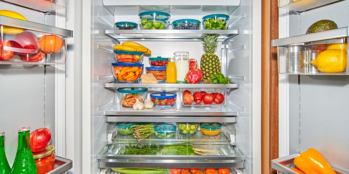 Open refrigerator neatly organized with fresh fruits, vegetables, and prepared foods stored in clear Anyday microwave-safe dishes with Kale green lids.