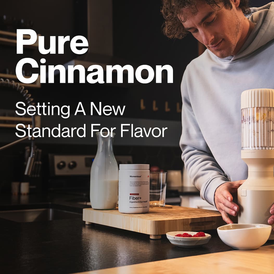 Man preparing a drink in a kitchen beside a container of Momentous Fiber+ with text reading: “Pure Cinnamon. Setting A New Standard For Flavor.”