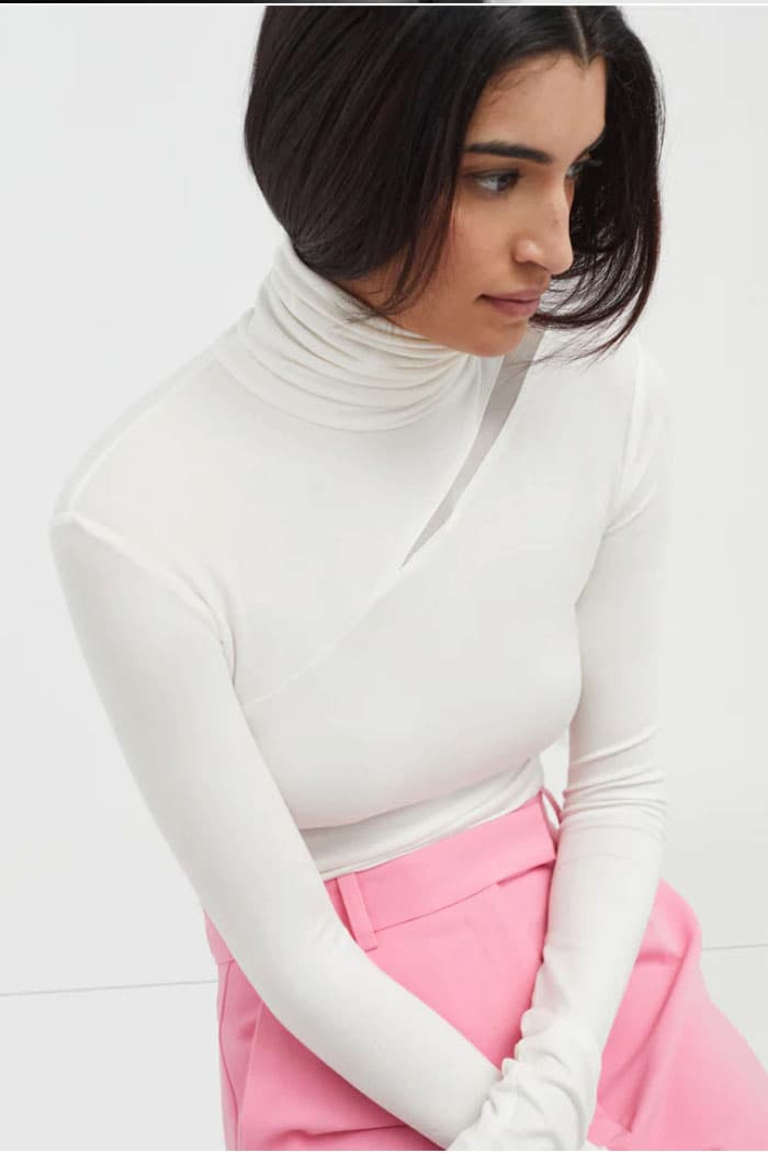Sam wears the Vee Top with a diagonal collarbone slit, paired with bright pink trousers.