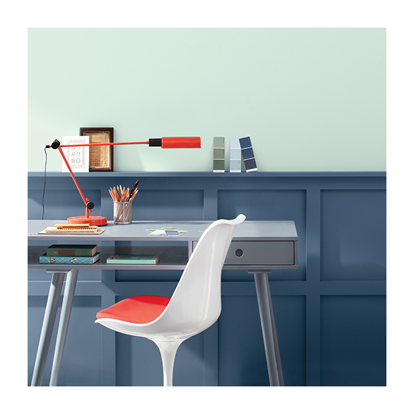 A home office with a light blue painted upper wall, dark blue wainscoting, a modern gray desk, and a white chair.