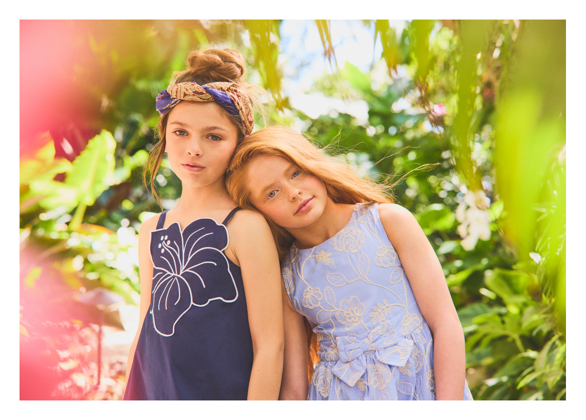 Two young girls in floral dresses posing outdoors among tropical greenery