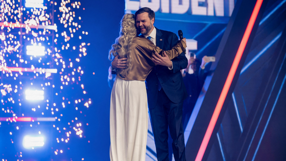 A man and a woman embrace on stage against a backdrop of blue light.