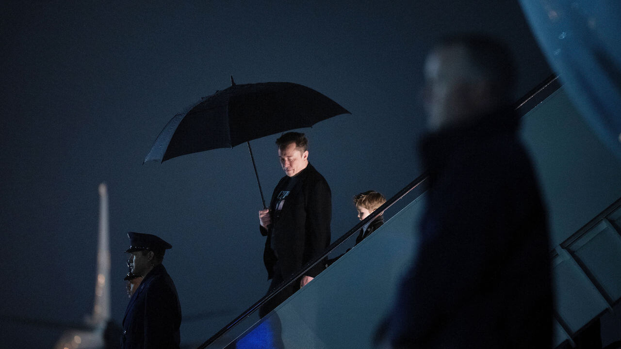 Elon Musk holds an umbrella as he and his son step off of Air Force One.