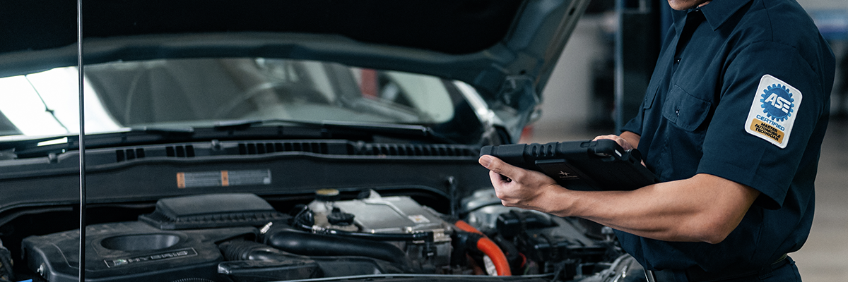 Technician with tablet near car with hood up