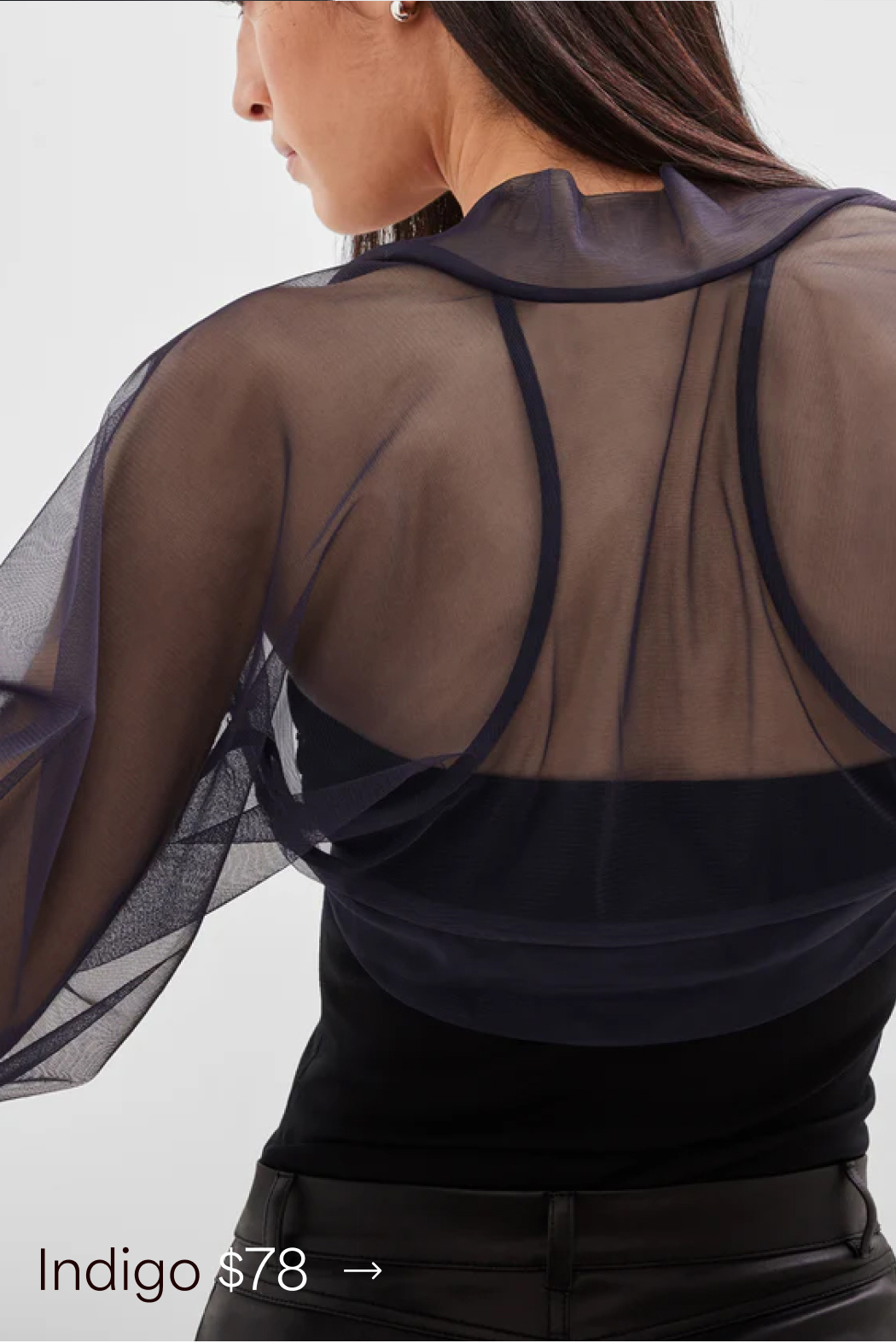 A close-up back view of Sam wearing an indigo The Olympia Bolero a black top, labeled “Indigo $78.”