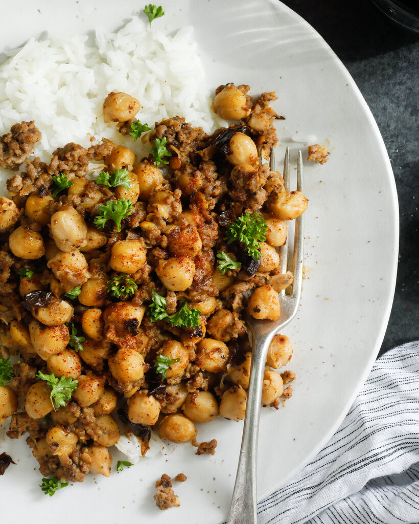 Seasoned chickpeas and beef on a bed of white rice, on a white plate.
