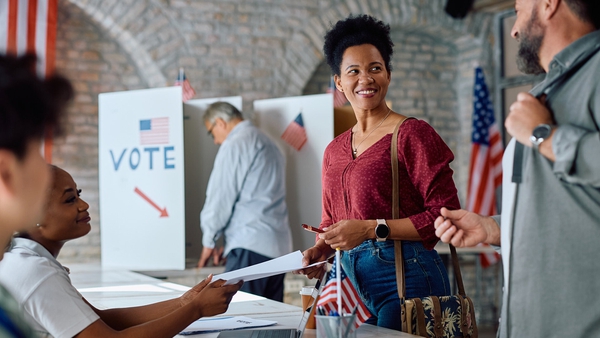 woman smiles while another woman hands her a paper at a polling place