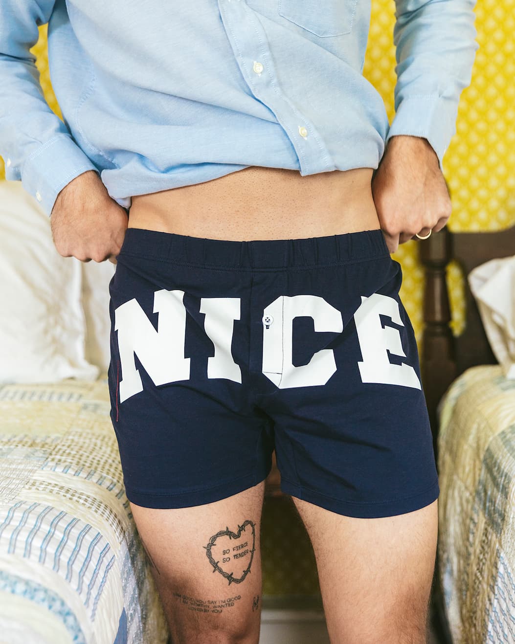 Close up of man lifting shirt to show his navy blue slim fit boxers with NICE written on front in white.