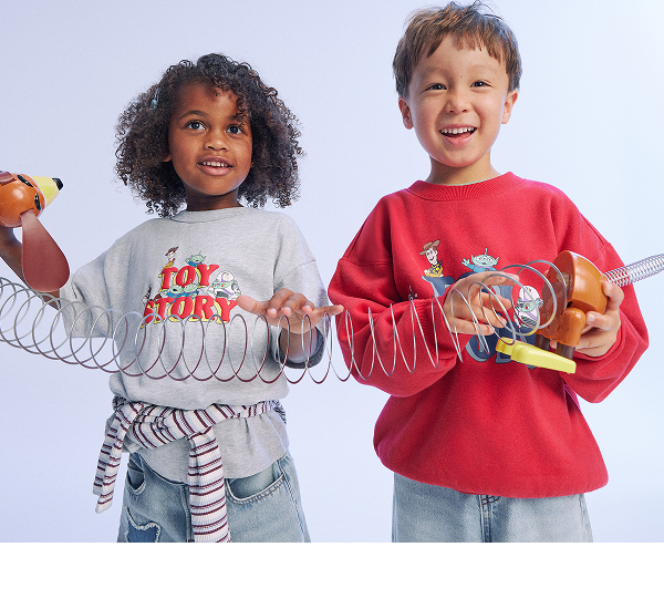 Two young children wearing Toy Story graphic t-shirts and jeans, holding toy guitars against a light blue background