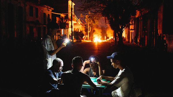 People illuminate themselves with their phones while playing dominoes as a fire set up by residents protesting against prolonged power outages burns on a street in Havana, Cub