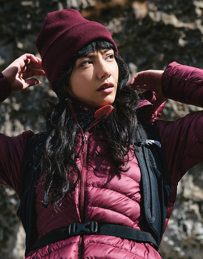 A woman wearing a maroon jacket and hat in a rocky landscape.