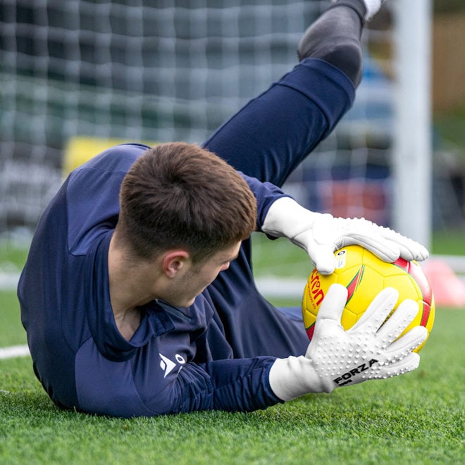 Goalkeeper wearing FORZA NGE Goalkeeper clubs, savinga a ball in front of goal.