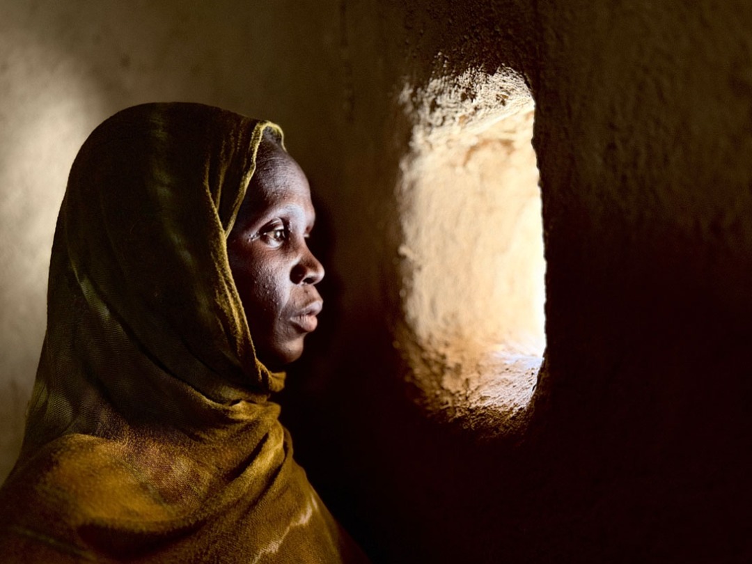 A woman with a headscarf is looking into the light through a hole in the wall.