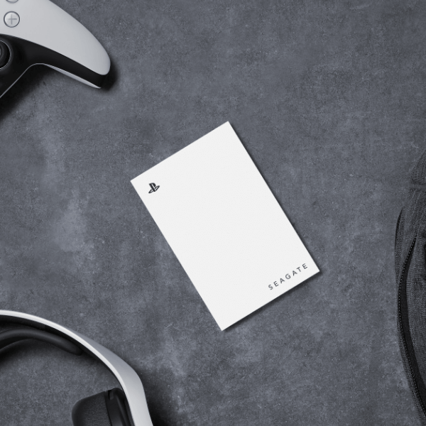 A white Seagate external hard drive with a PlayStation logo sits on a dark surface, surrounded by a black gaming controller and headphones.