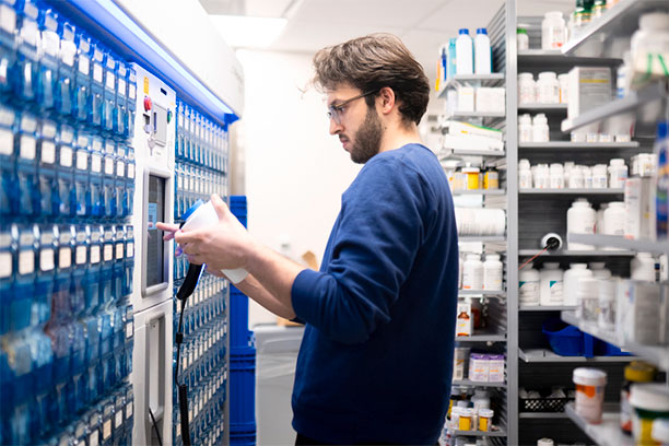 A patient with a prescription looks at a row of automated holders for medication.