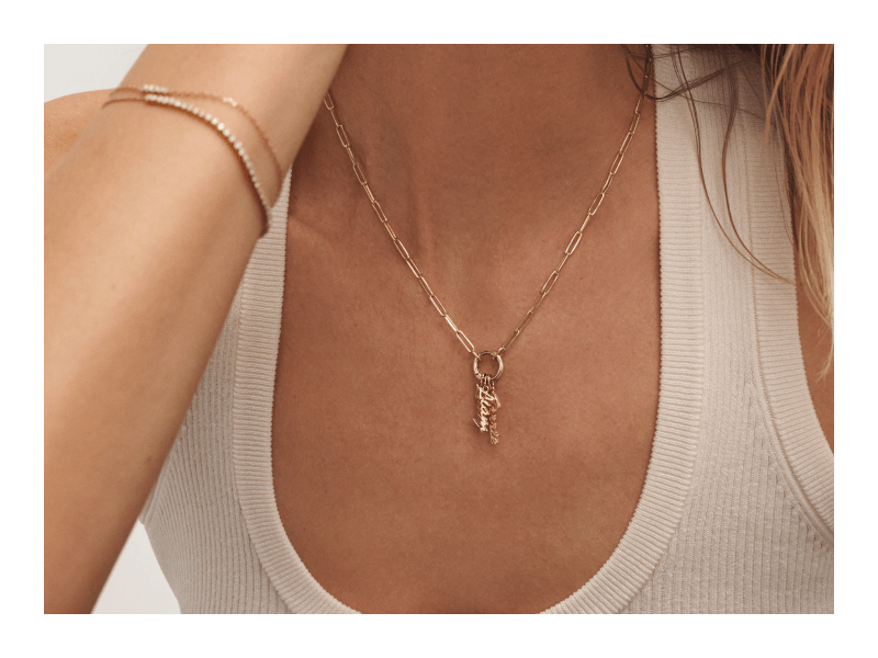A model wearing a gold paperclip chain necklace with sparkling letter charms, and bracelets.