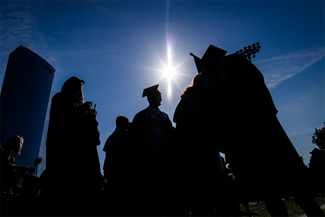 The sun casts a silhouette on students in graduation robes.