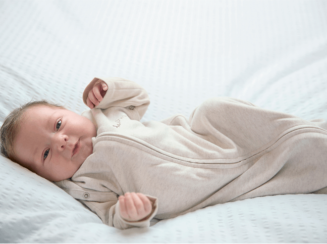 Baby lay, smiling, wearing the oatmeal style swaddle with the arms free mode