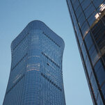 A close-up of two modern skyscrapers made of glass. One building has a distinct curved shape, the other reflects light.