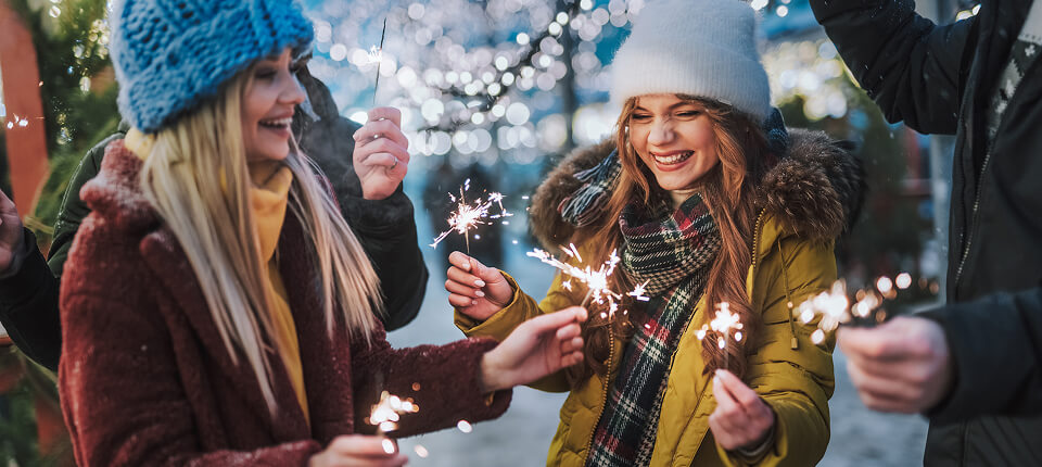 A family plays with sparklers against a background of twinkling seasonal lights.
