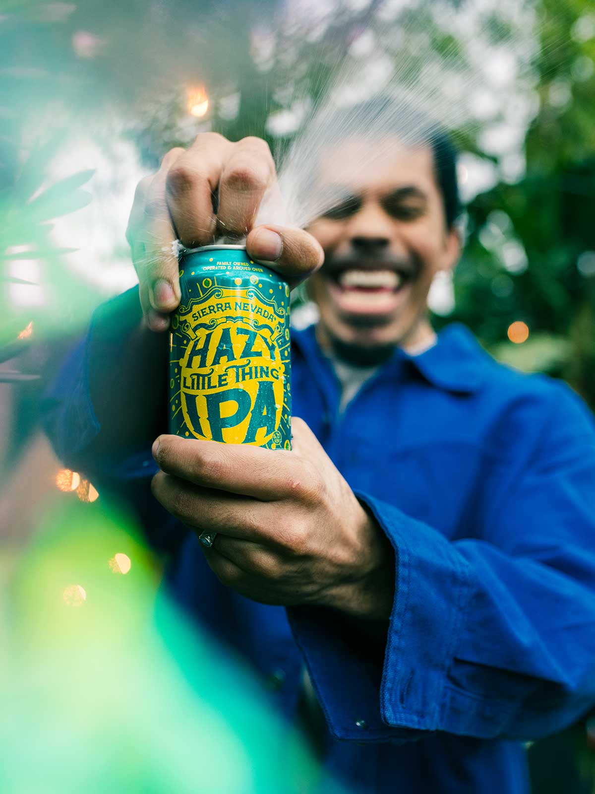 A man, surrounded by trees, opening a can of Hazy Little Thing IPA