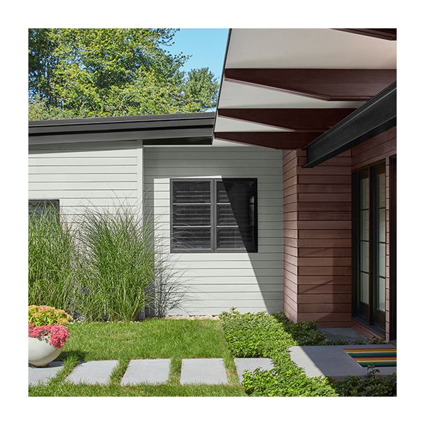 A light gray painted home exterior with rafters casting shade over the lawn.
