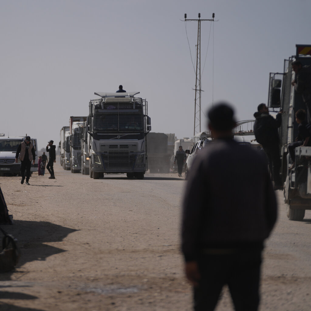 A man seen from behind watches a convoy of trucks approaching.