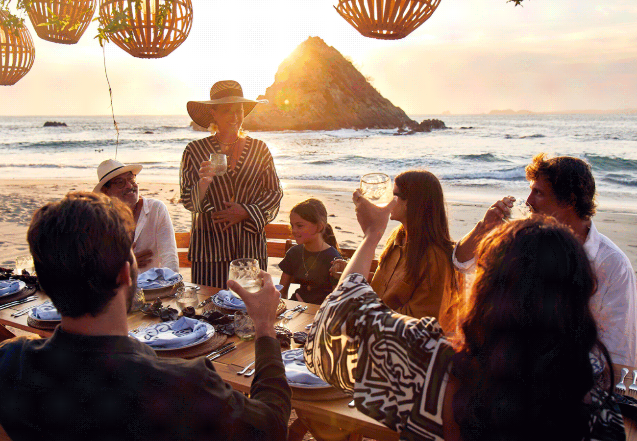 Hero GIF featuring four frames 1) A group surrounding a table on the beach enjoying drinks as they wait for their meal. 2) A group of people sitting on a boat in the ocean. 3) A tall festively decorated Christmas tree illuminated with lights, set against a sky backdrop with clouds. 4) A group of people walking towards the beach.