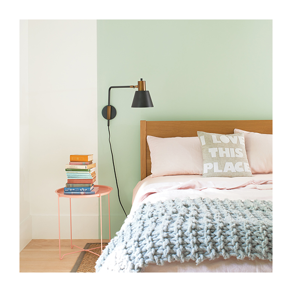 A white bedroom with a seafoam green painted square behind a wooden bed.