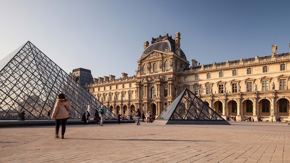 Image description: People walking outside the Louvre Museum in Paris.
