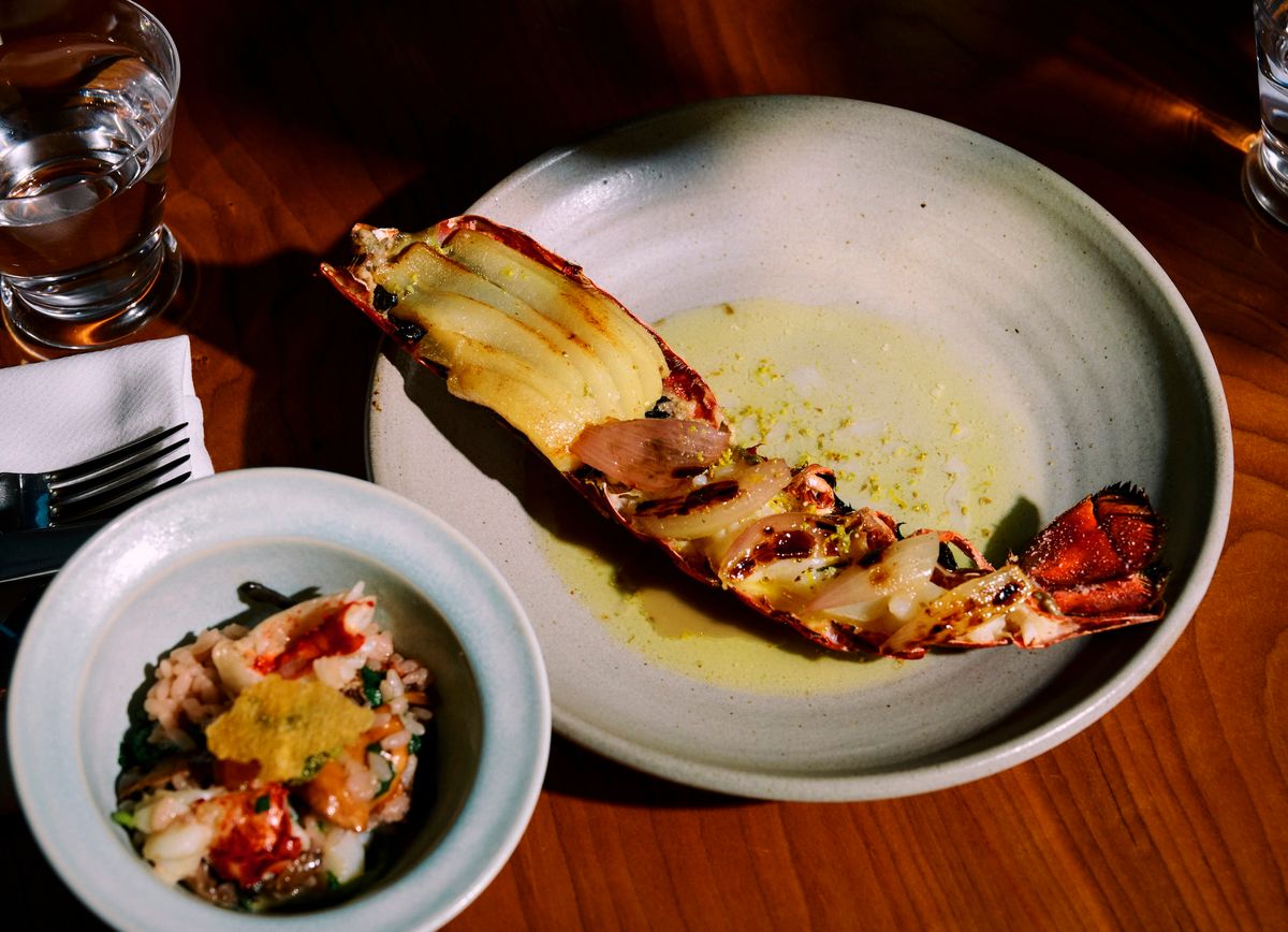 A plate of a half grilled lobster next to a small bowl of lobster and rice.