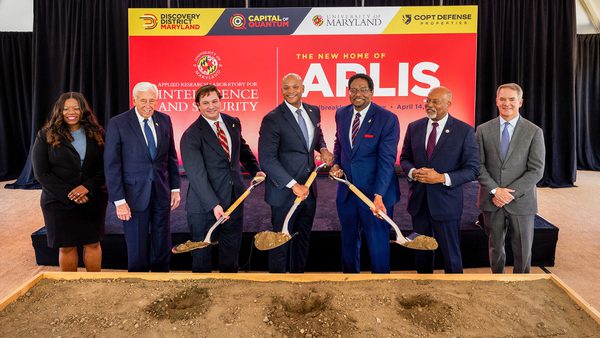 Seven people line up, three hoisting shovels, at a groundbreaking ceremony