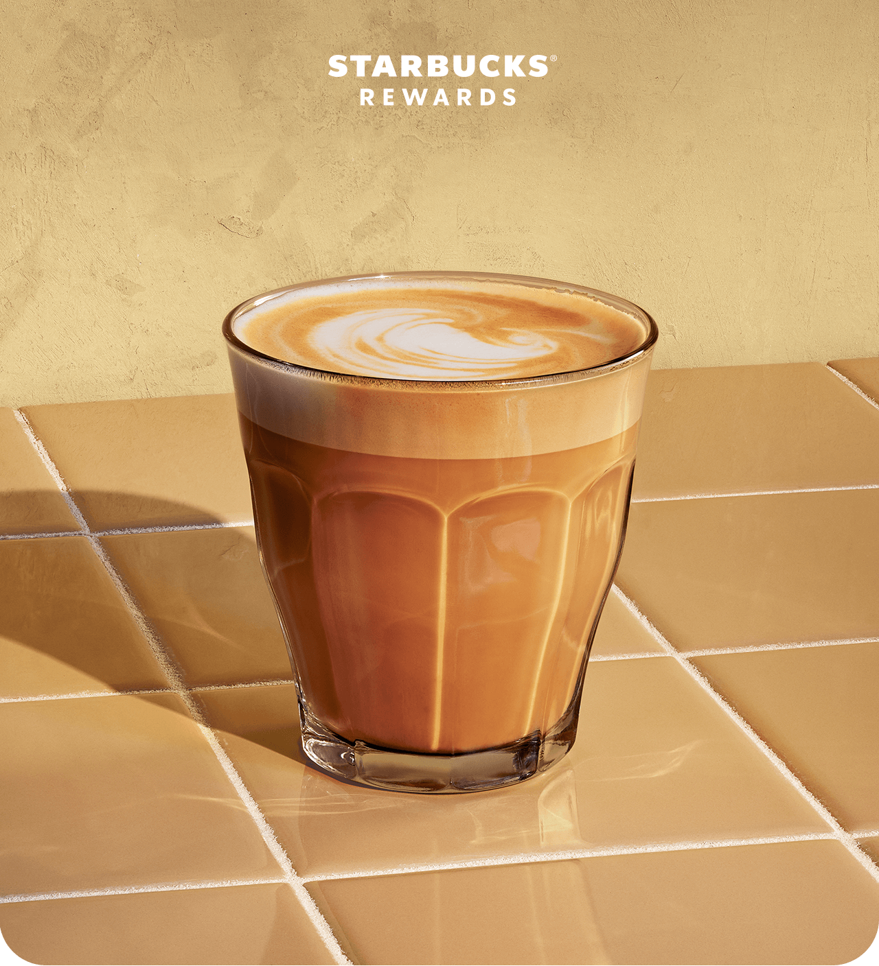 Starbucks&reg; Rewards | A cortado sitting in a glass cup on a warm yellow tiled backdrop.