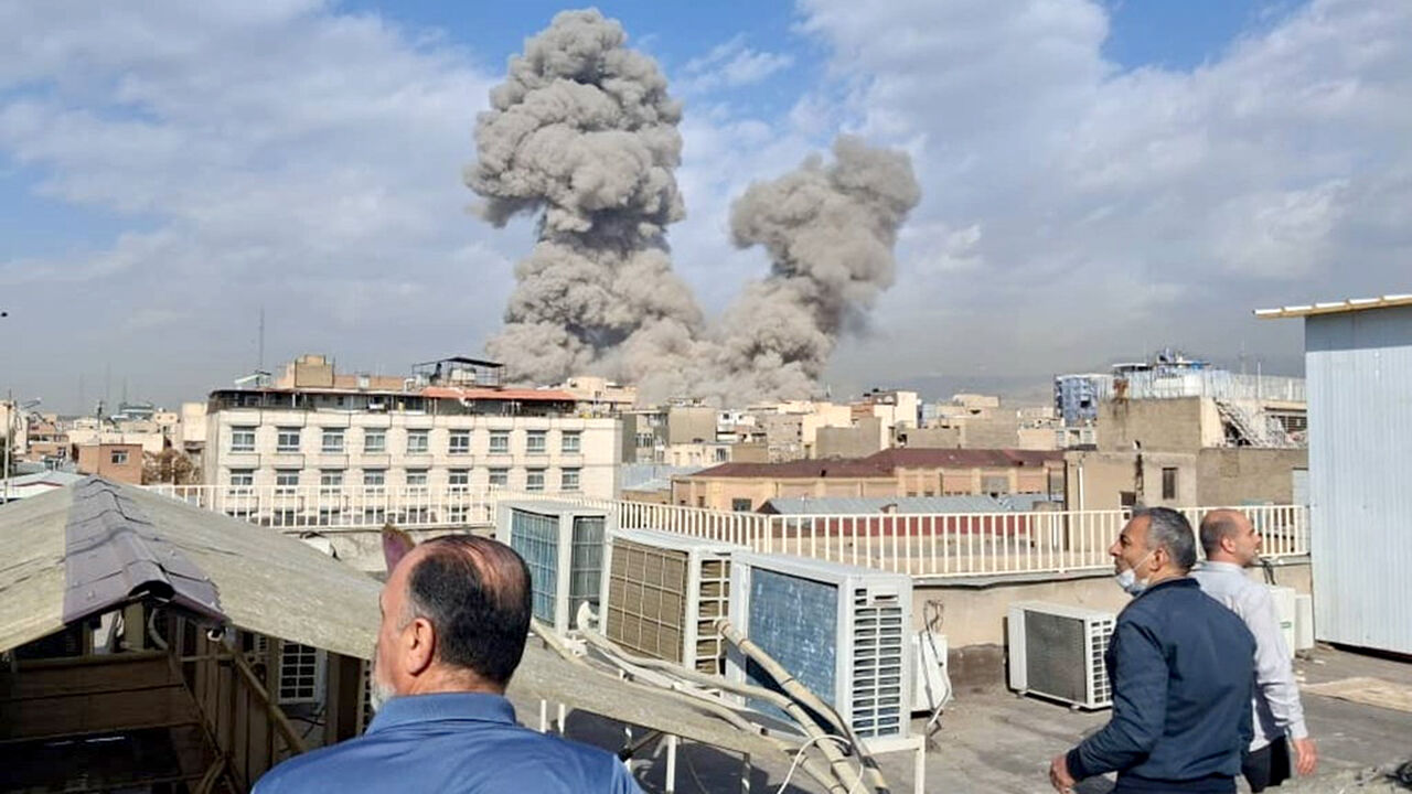 People watch as smoke rises on the skyline after an explosion in Tehran, Iran