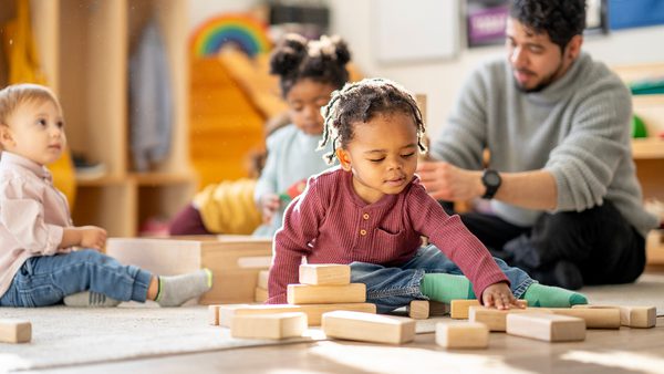 three young children play with blocks as caregiver watches them