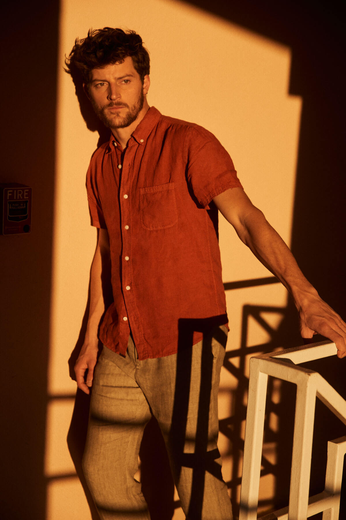 Model wears red linen button-down shirt and brown trousers