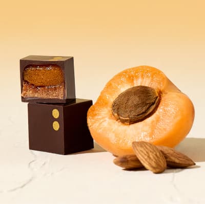 Two Apricot & Almond bonbons next to a fresh apricot and a handful of almonds.