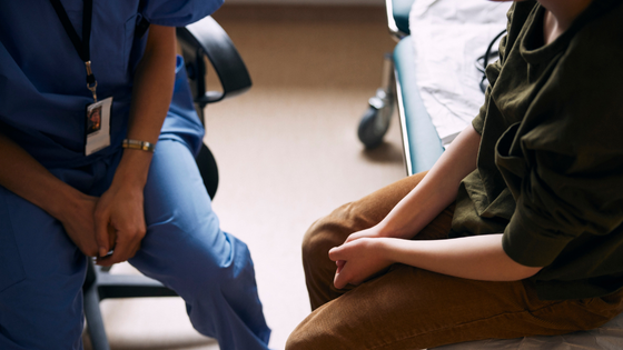 A person with scrubs sits with a patient.