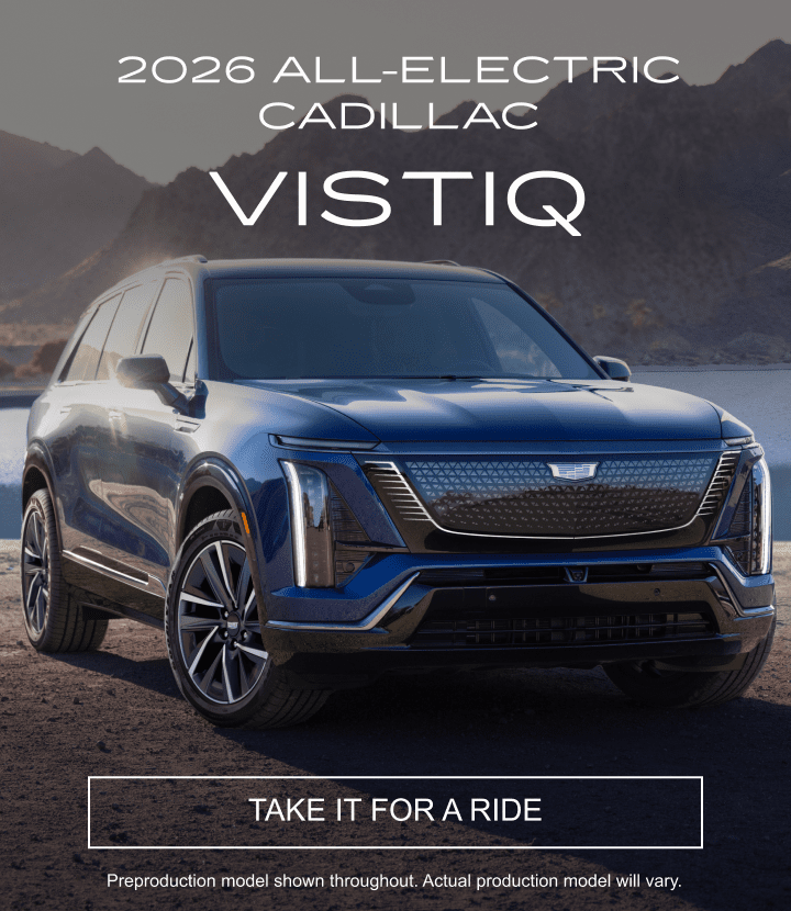 2026 Cadillac VISTIQ parked on a rocky road by a lake with mountains in the background.