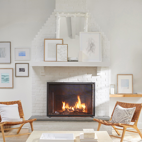 A white wall with framed artwork and white-painted brick fireplace flanked by matching leather and wood chairs.