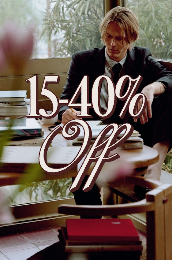 15–40% Off. Man in a suit sitting by a window surrounded by stacks of books.