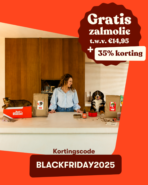 Een vrouw staat lachend in de keuken tussen haar hond en kat. Op het aanrecht staan zakken dierenvoer en een Just Russel-doos. Tekst: “35% korting + gratis zalmolie t.w.v. €14,95. Kortingscode BLACKFRIDAY2025.”