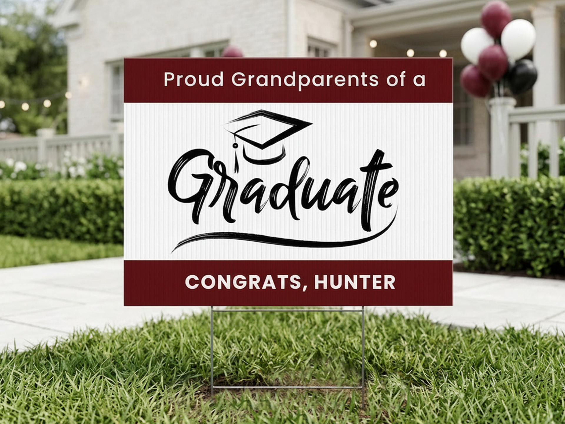 Graduation yard sign reading ‘Proud Grandparents of a Graduate, Congrats Hunter’ displayed on lawn in front of house with celebration balloons