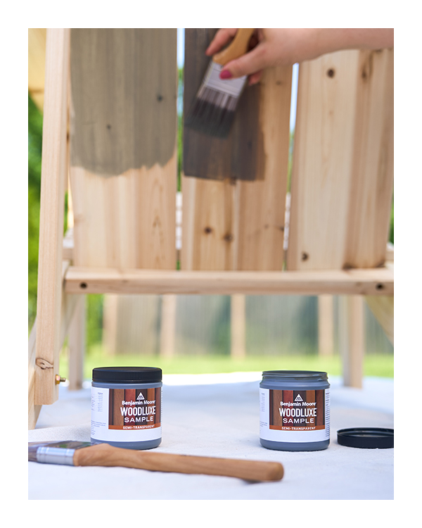 A person samples two different shades of brown Woodluxe Exterior Stains on the back of a wooden chair.