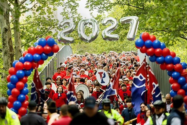 A procession of third-years in red shirts and mock skimmer hats passes under 2027 balloon numbers for Hey Day.