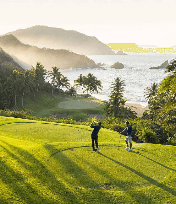 Golf course with two people on a grassy hill, overlooking oceanfront views.