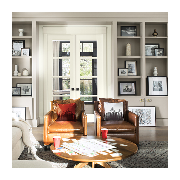 A comfy living room with gray-painted built-in bookshelves, white french doors, a white sofa, and brown leather chairs.
